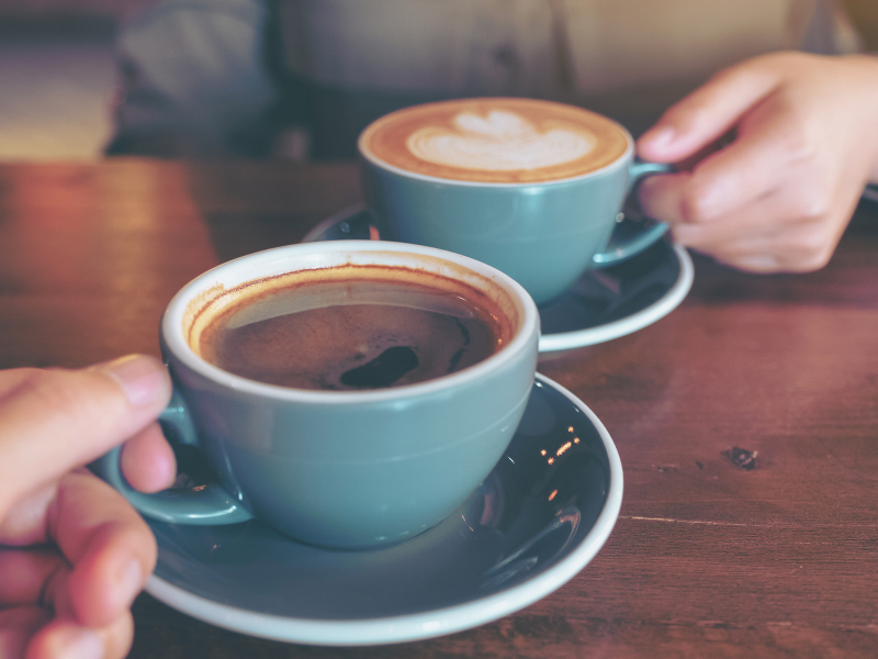 Two people having coffees at a meeting. Mugs are a teal ceramic