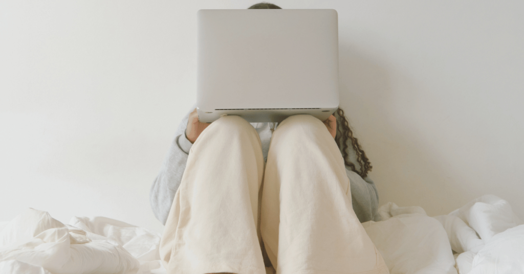 a woman sits against a wall with a laptop on her knees, entrepreneur burnout for female founders