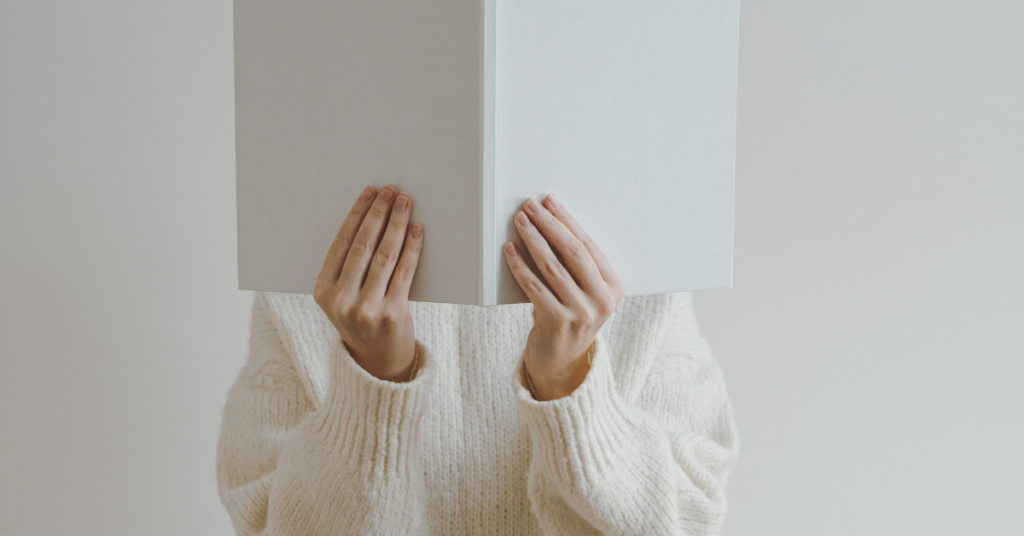 A woman holds a blank book in front of her face